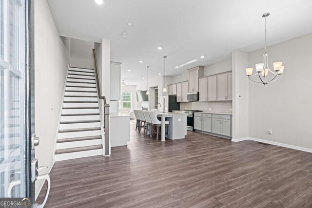 kitchen with gray cabinetry, hanging light fixtures, a kitchen breakfast bar, an island with sink, and appliances with stainless steel finishes