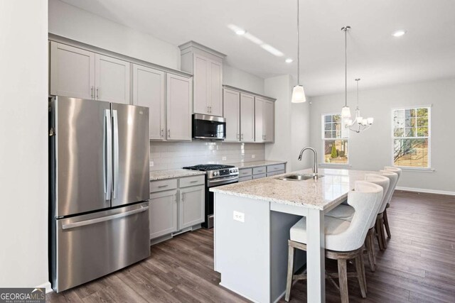 kitchen featuring light stone countertops, stainless steel appliances, a kitchen island with sink, sink, and gray cabinets