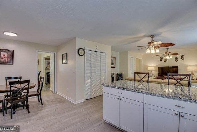 kitchen featuring ceiling fan, light stone counters, white cabinetry, and light wood-type flooring