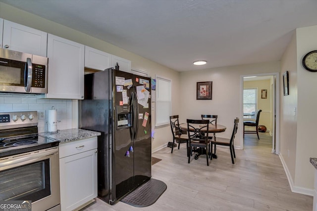 kitchen with tasteful backsplash, white cabinets, stainless steel appliances, and light hardwood / wood-style floors