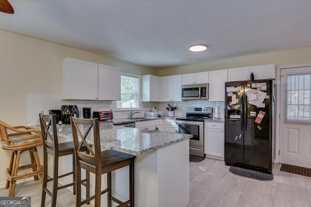 kitchen featuring white cabinets, a kitchen bar, kitchen peninsula, and stainless steel appliances