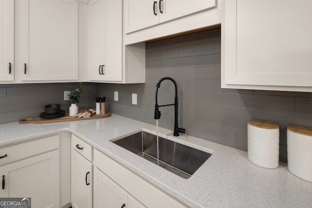 kitchen featuring light stone countertops, tasteful backsplash, white cabinetry, and sink