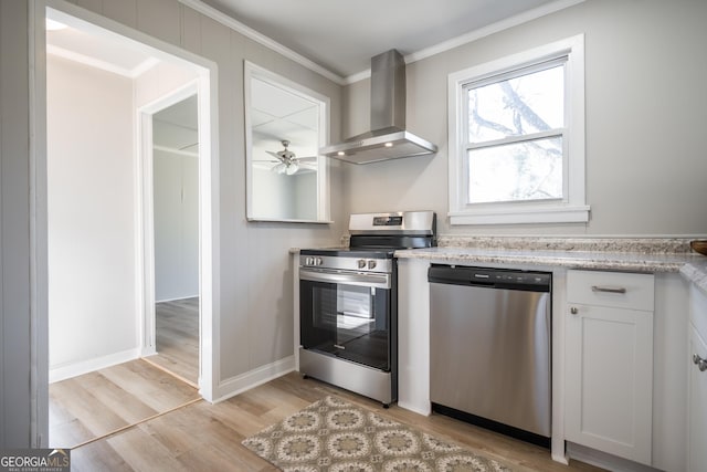 kitchen featuring white cabinetry, ceiling fan, stainless steel appliances, wall chimney range hood, and light wood-type flooring