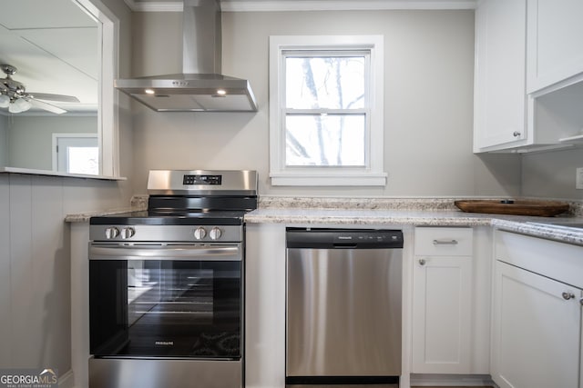 kitchen with wall chimney exhaust hood, ceiling fan, appliances with stainless steel finishes, light stone counters, and white cabinetry