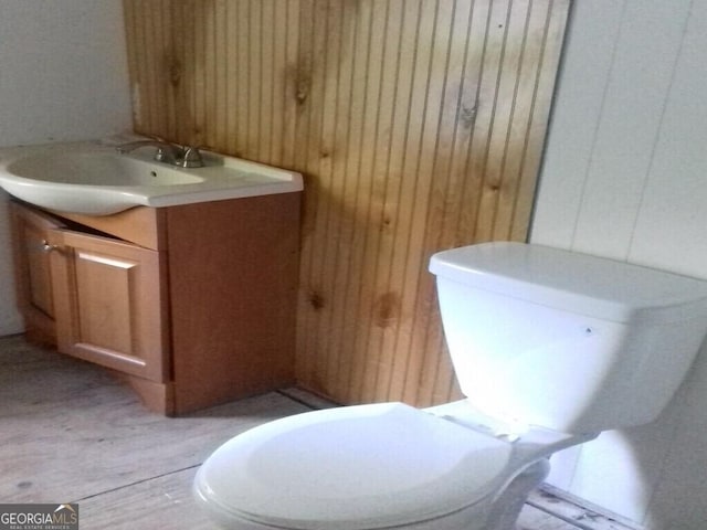 bathroom with toilet, wooden walls, and vanity