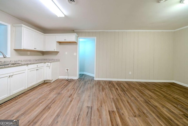 kitchen featuring light stone countertops, crown molding, sink, white cabinets, and light hardwood / wood-style floors