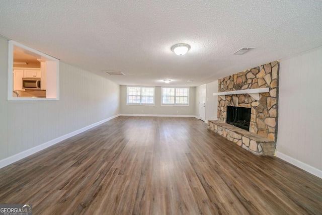 unfurnished living room with a textured ceiling, dark hardwood / wood-style flooring, and a stone fireplace