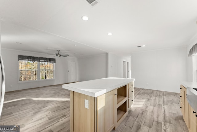 kitchen with a center island, ceiling fan, light wood-type flooring, ornamental molding, and light brown cabinetry