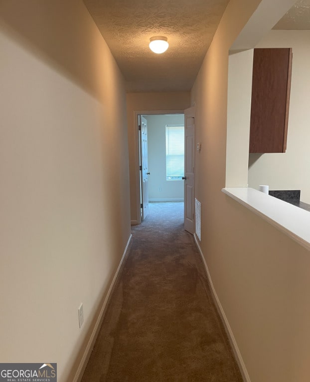 corridor with dark carpet and a textured ceiling