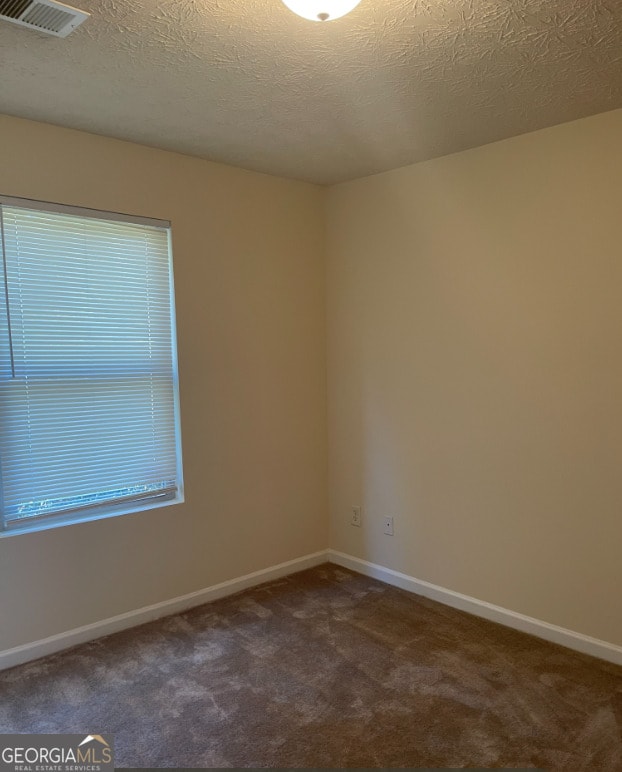 unfurnished room with a textured ceiling and dark carpet