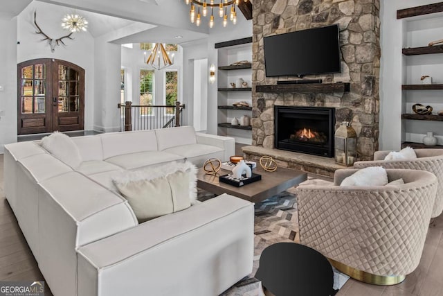 living room featuring french doors, hardwood / wood-style flooring, built in shelves, a fireplace, and a notable chandelier