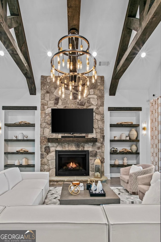 living room with a notable chandelier, beam ceiling, and a stone fireplace