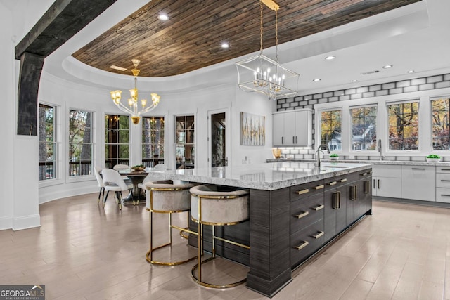 kitchen featuring white cabinetry, a large island, a tray ceiling, and decorative light fixtures