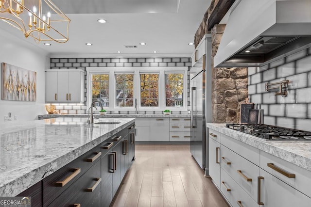 kitchen featuring white cabinets, sink, light stone countertops, decorative light fixtures, and custom range hood