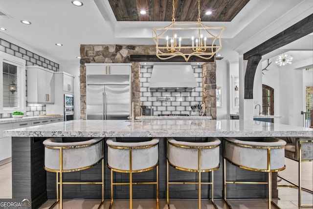 kitchen with white cabinetry, a kitchen breakfast bar, light stone counters, stainless steel built in refrigerator, and a spacious island