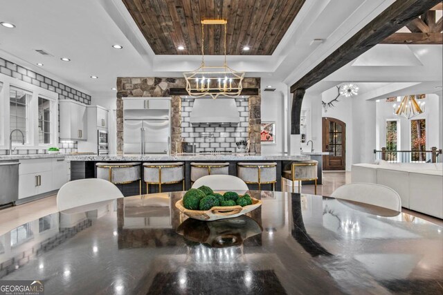 interior space featuring a kitchen breakfast bar, built in appliances, white cabinetry, and hanging light fixtures