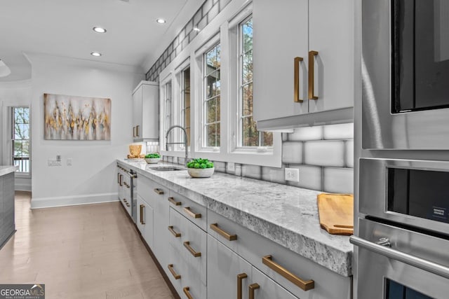 kitchen with light stone counters, white cabinetry, plenty of natural light, and sink