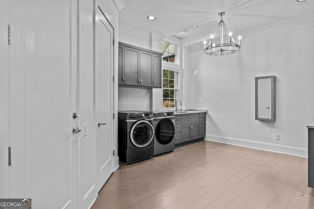 laundry room with cabinets, crown molding, light hardwood / wood-style flooring, a notable chandelier, and washing machine and dryer