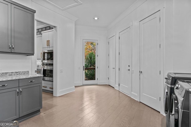 kitchen with gray cabinetry, stainless steel double oven, light stone counters, washer and dryer, and light wood-type flooring