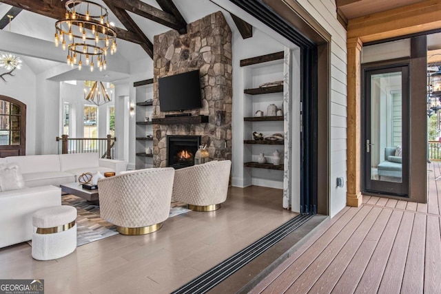 living room featuring wood-type flooring, built in features, an inviting chandelier, vaulted ceiling with beams, and a stone fireplace