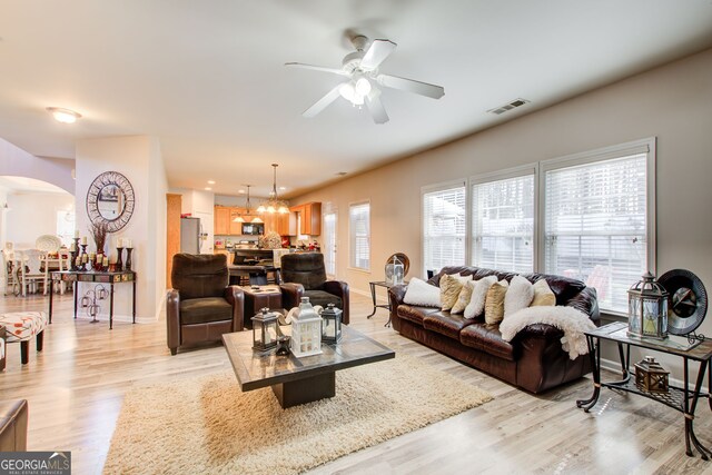 living area featuring visible vents, baseboards, arched walkways, light wood-style floors, and ceiling fan with notable chandelier