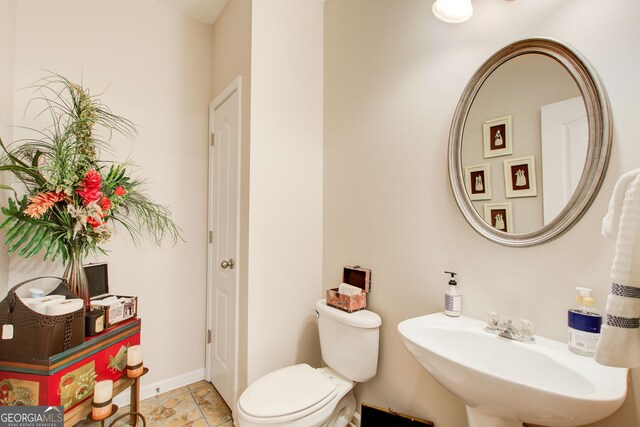 half bathroom featuring tile patterned flooring, toilet, baseboards, and a sink