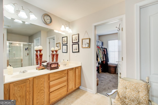 full bath featuring double vanity, a stall shower, baseboards, and a sink