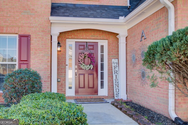 property entrance featuring brick siding and a shingled roof