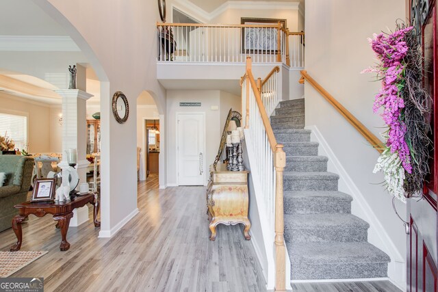 foyer featuring wood finished floors, arched walkways, a high ceiling, and ornamental molding