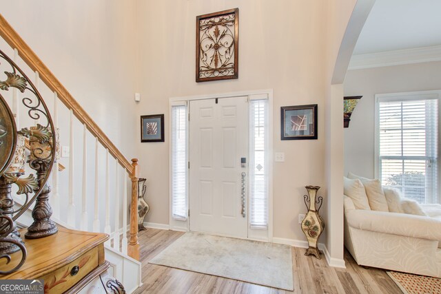 entrance foyer with light wood finished floors, baseboards, stairway, ornamental molding, and arched walkways