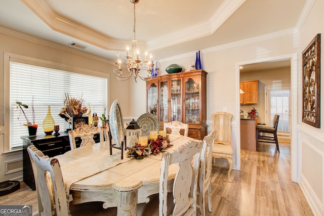 dining space featuring an inviting chandelier, a tray ceiling, a healthy amount of sunlight, and light wood finished floors