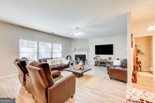 living room with a glass covered fireplace, light wood-style flooring, and a ceiling fan