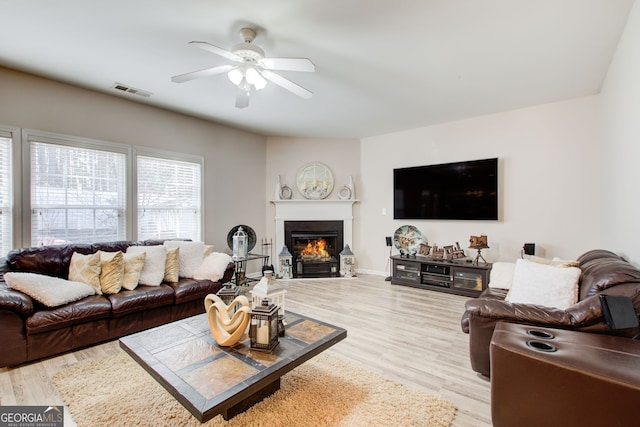 living room with ceiling fan, visible vents, a glass covered fireplace, and wood finished floors