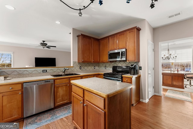 kitchen featuring ceiling fan with notable chandelier, appliances with stainless steel finishes, a center island, sink, and light wood-type flooring