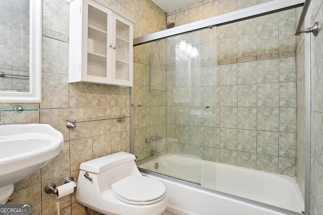 bathroom featuring toilet, tile walls, and bath / shower combo with glass door