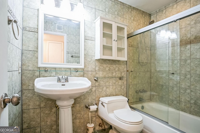 bathroom with backsplash, toilet, combined bath / shower with glass door, and tile walls