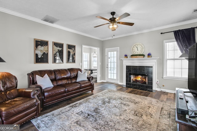 living room featuring a tiled fireplace, crown molding, and dark wood-type flooring