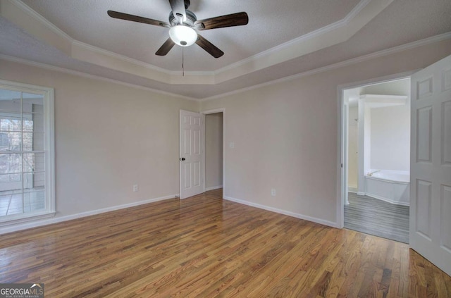 empty room featuring hardwood / wood-style flooring, ceiling fan, a raised ceiling, and ornamental molding