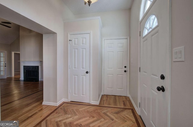 entryway with ceiling fan, a fireplace, and light parquet floors