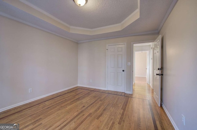 empty room featuring hardwood / wood-style floors, crown molding, a raised ceiling, and a textured ceiling