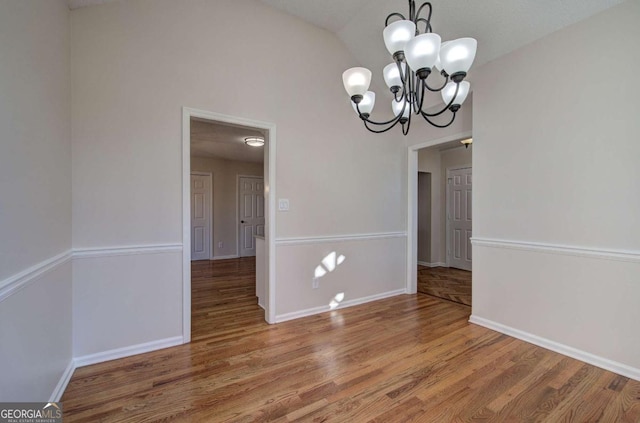 unfurnished dining area featuring hardwood / wood-style flooring, an inviting chandelier, and vaulted ceiling