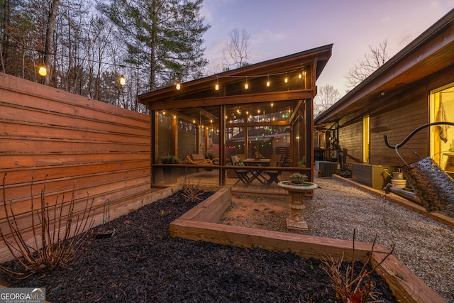 back house at dusk featuring a patio, a sunroom, and central AC