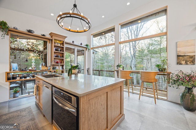 kitchen featuring sink, decorative light fixtures, a center island with sink, stainless steel dishwasher, and a notable chandelier