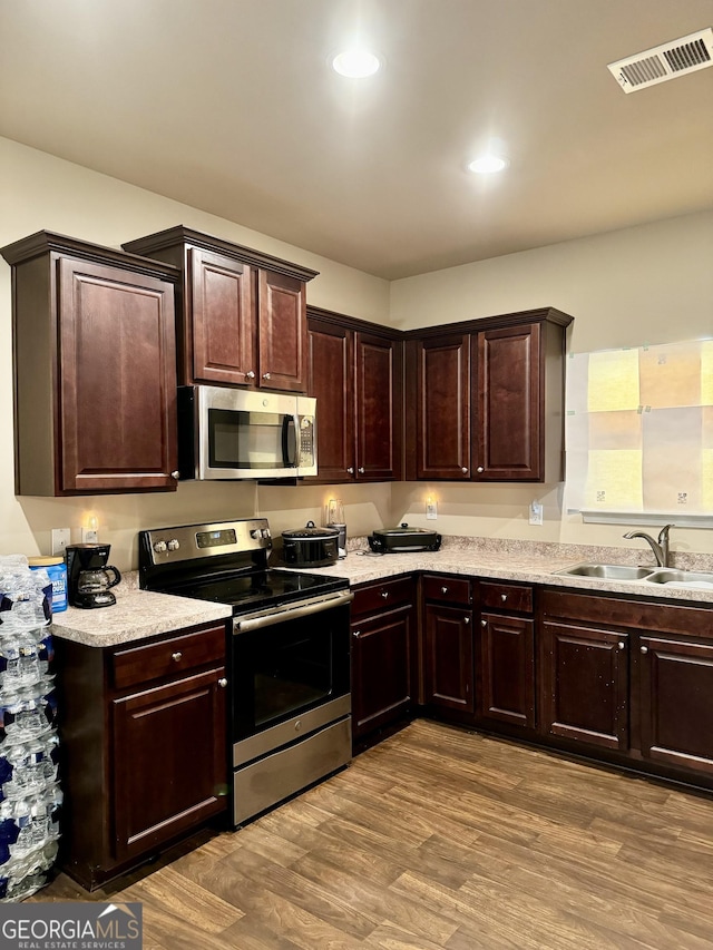 kitchen with dark brown cabinetry, sink, stainless steel appliances, and light hardwood / wood-style floors