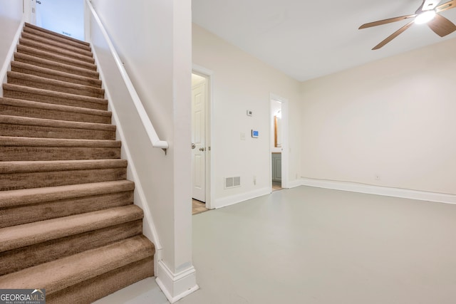 stairs with ceiling fan and concrete floors