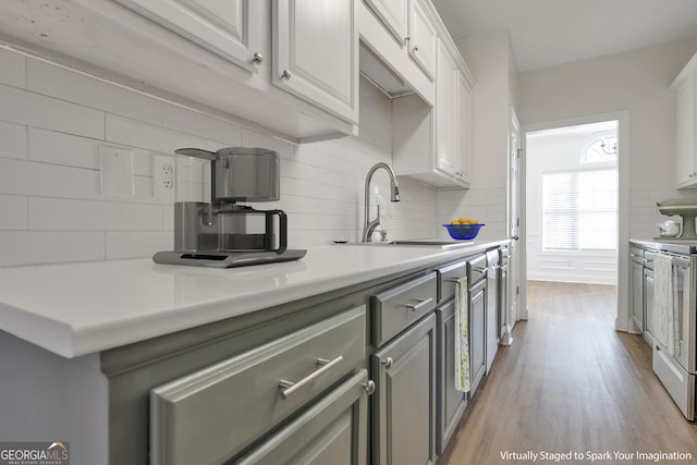 kitchen with white electric range, sink, tasteful backsplash, light hardwood / wood-style floors, and white cabinetry