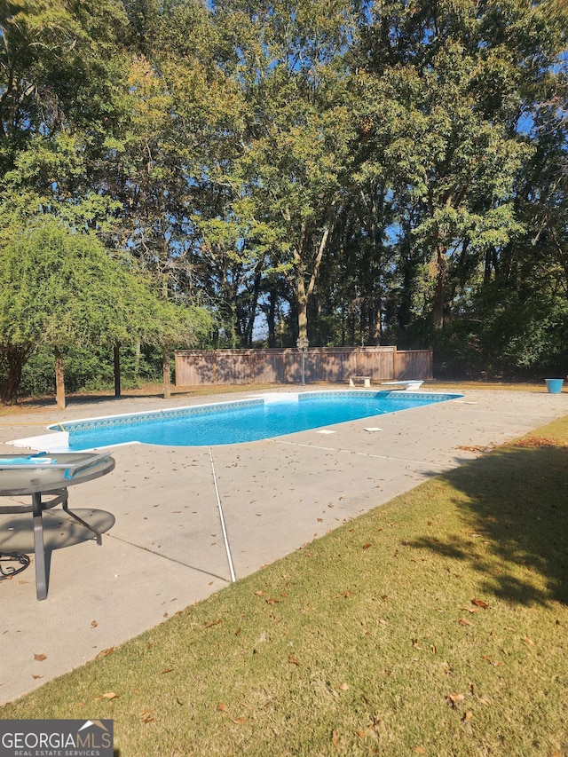 view of swimming pool featuring a yard, a patio, and a diving board