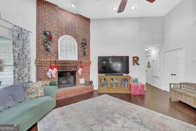 living room featuring ceiling fan, dark hardwood / wood-style flooring, a towering ceiling, and a brick fireplace