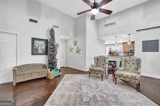 living area featuring a towering ceiling, dark hardwood / wood-style floors, and ceiling fan