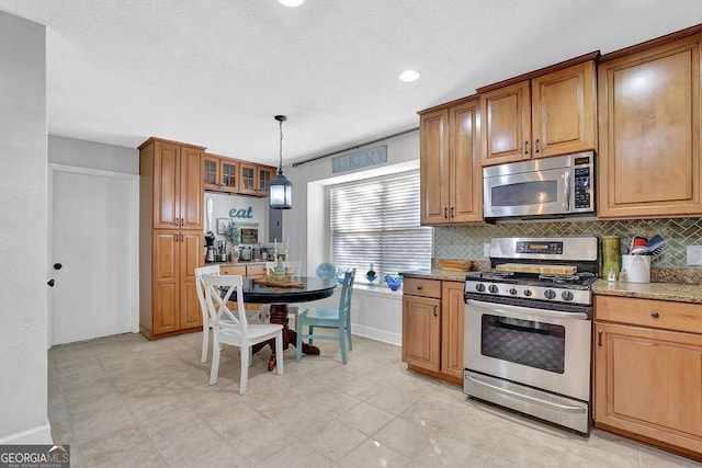 kitchen with light stone countertops, hanging light fixtures, appliances with stainless steel finishes, and tasteful backsplash